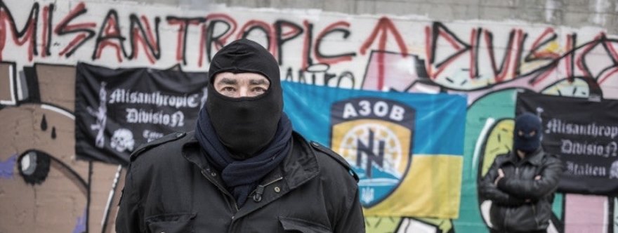 El entrevistado por la televisión suiza, probablemente Saverio Fontana, con banderas de Azov y la Misanthropic Division al fondo. 